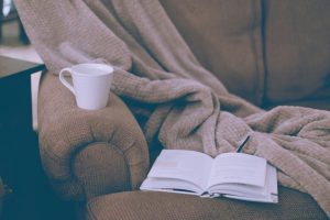 A cozy setting in a chair with a blanket, tea and a book